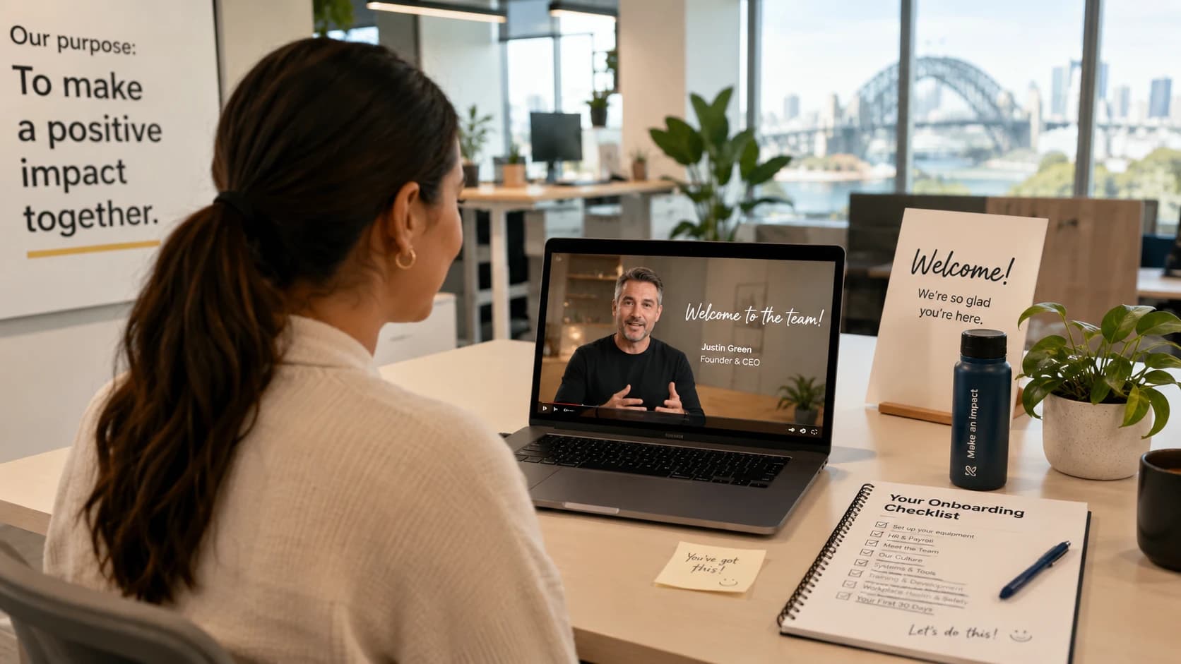 New employee at her first-day desk watching a welcome video from the company founder on her laptop